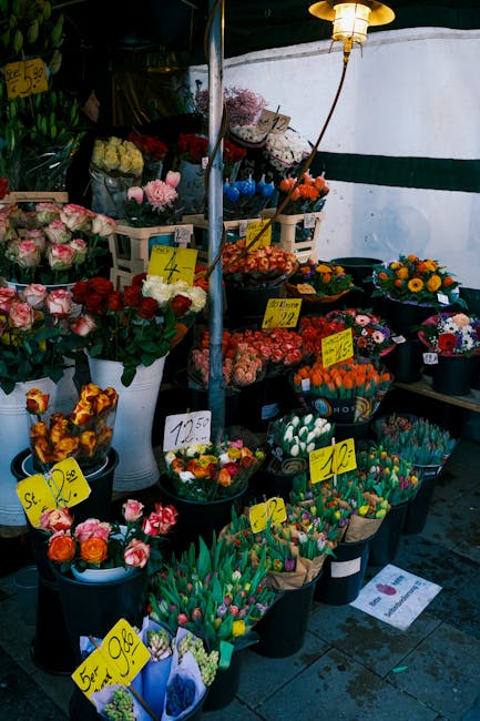 An outdoor flower stall displaying a vibrant assortment of fresh floral arrangements and bouquets. The arrangement includes roses, tulips, and chrysanthemums in various colors such as pink, red, orang