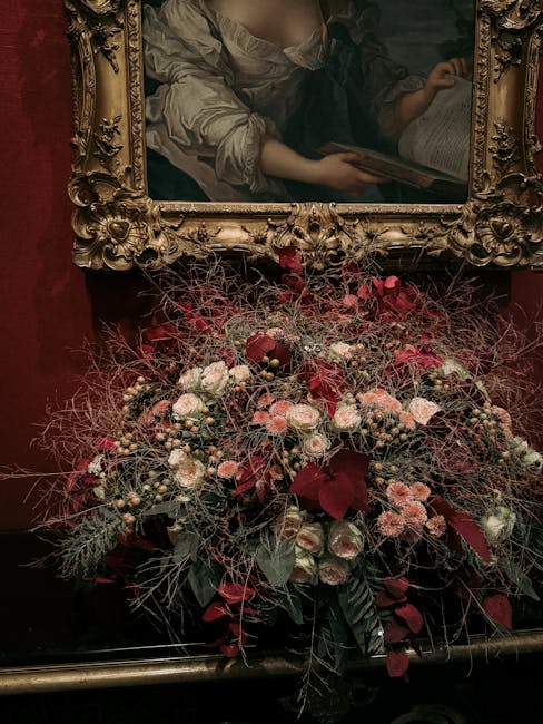 A lush floral arrangement featuring a variety of fresh flowers, including soft pink roses, deep red blooms, and smaller pale pink blossoms, complemented by dark green and burgundy foliage. The bouquet