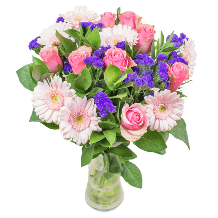 A striking and elegant floral arrangement, meticulously designed in the style admired by Mayfair's discerning clientele, is displayed in a pristine clear glass vase against a pure white backdrop. Centered within the bouquet, approximately seven to nine pink roses-some gently furled, others just beginning their classic spiral unfurling-establish a sense of timeless romance. These are complemented by five to seven pale pink gerbera daisies, their large, daisy-like heads and countless petals revealing delicate, almost white centres. Clusters of vivid purple statice flowers, likely sourced from a trusted local supplier near Grosvenor Street, are interspersed throughout, offering a textured counterpoint and vibrant colour accent. The base of luxuriant deep green foliage not only adds volume and balance but brings the essence of Mayfair's lush green squares into the room. The transparent vase displays neatly arranged stems in crystal-clear water, underscoring the bouquet's freshness and artful presentation. Perfect for birthdays, anniversaries, or as an elegant accent for a Mayfair office, this arrangement of pink roses, gerberas, and purple fillers communicates joy, thoughtfulness, and lasting affection-a sentiment echoed in the bespoke floral artistry found across this iconic neighbourhood.